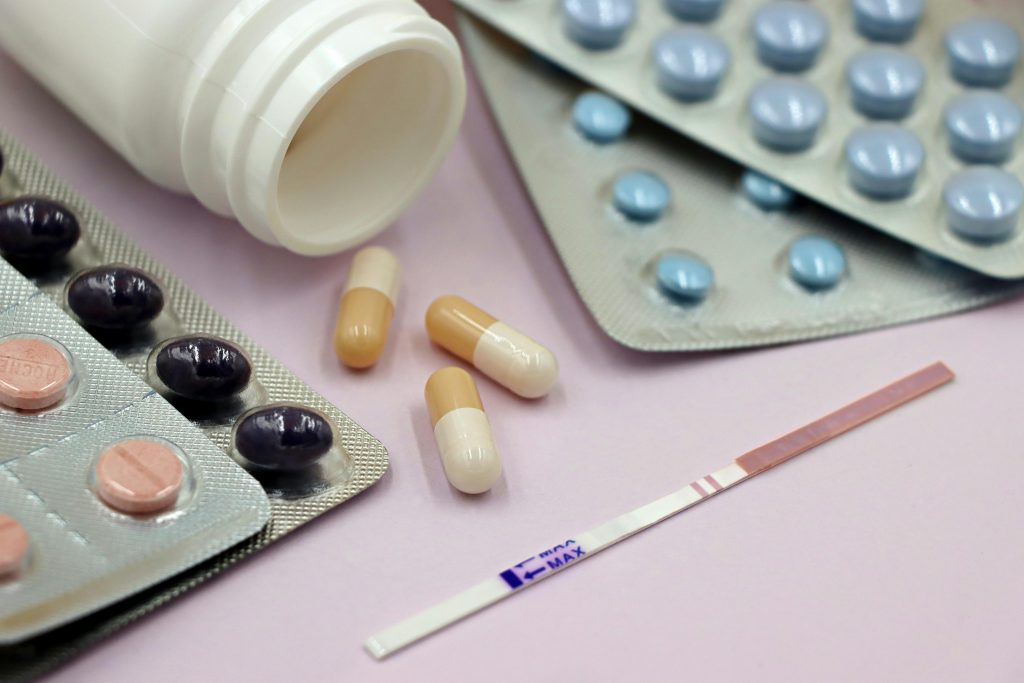 pexels-photo-28153356-28153356 Image featuring a pregnancy test strip surrounded by various pills and capsules on a pastel background.