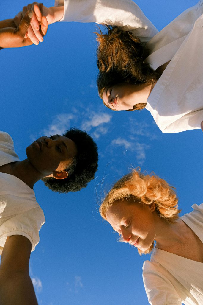 pexels-photo-4672553-4672553 Three women holding hands under a clear blue sky, symbolizing unity and friendship.
