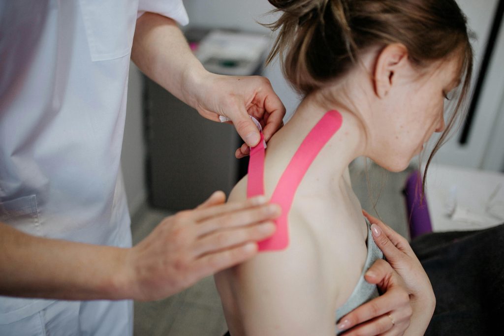 pexels-photo-8219055-8219055 A physiotherapist applies kinesio tape to a woman's shoulder for pain relief and treatment.